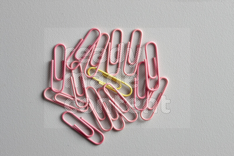 A yellow paperclip surrounded by bunch of pink paperclips on grey background