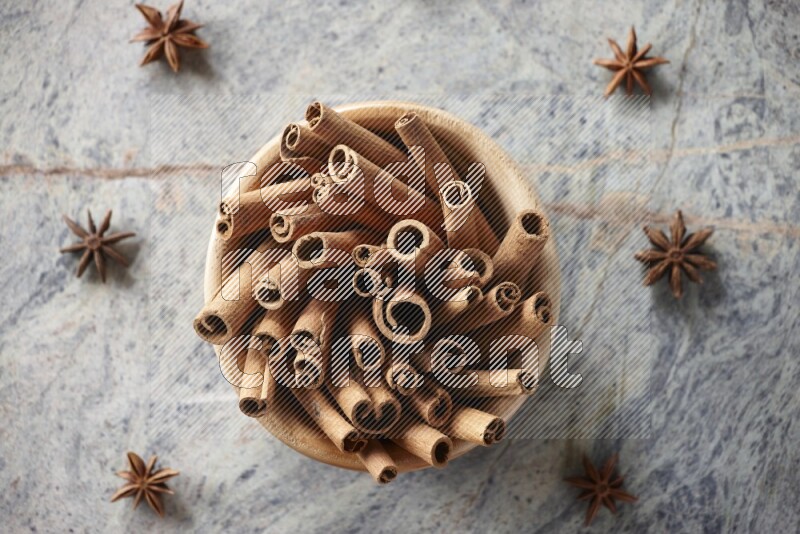 wooden bowl full of cinnamon sticks surrounded by star anis on marble background in different angles
