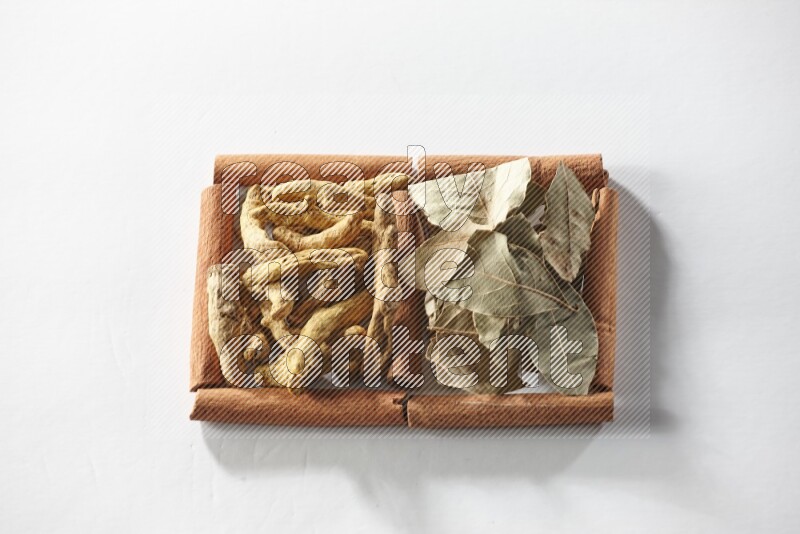 مربعان من أعواد القرفة ممتلئان بأصابع الكركم وأوراق الغار علي خلفية بيضاء