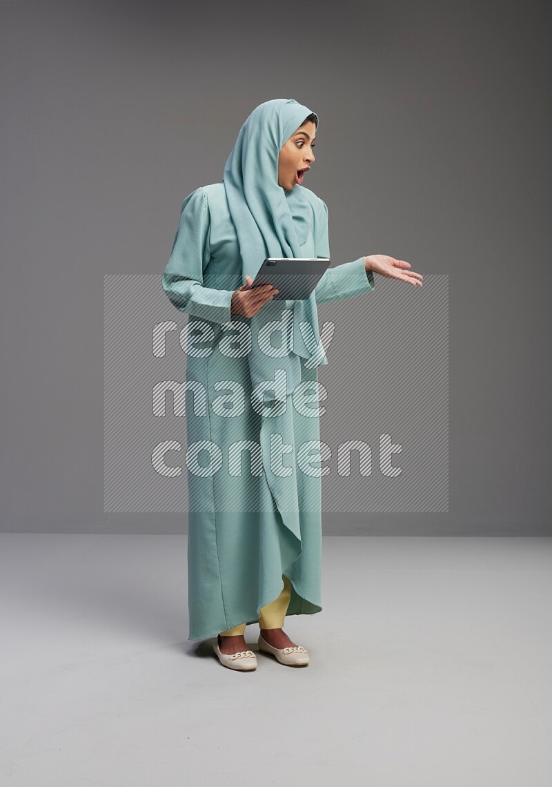 Saudi Woman wearing Abaya standing working on tablet on Gray background