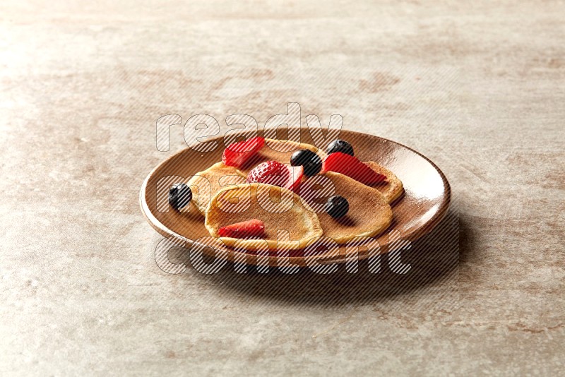 Five stacked mixed berries mini pancakes in a brown plate on beige background