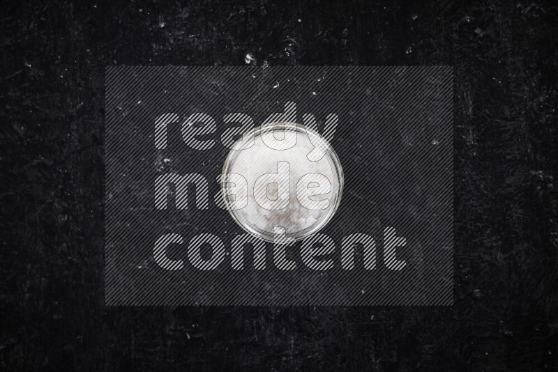 A glass jar full of coarse sea salt crystals on black background