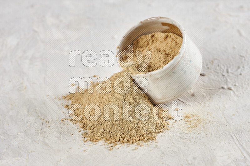 A beige pottery bowl full of ground ginger powder with fallen powder from it on white background