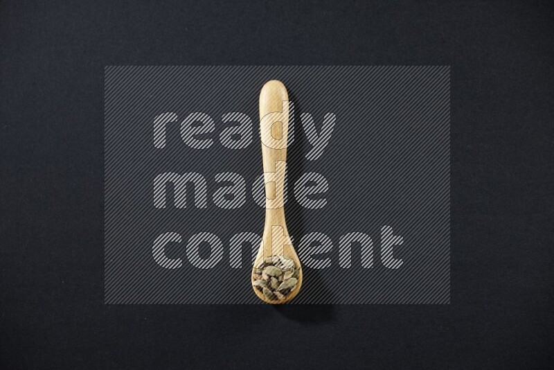 A wooden spoon full of cardamom on black flooring