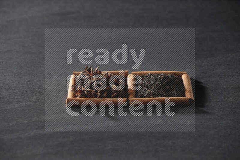 مربعان من أعواد القرفة ممتلئان باليانسون النجمي والشاي الأسود علي خلفية سوداء