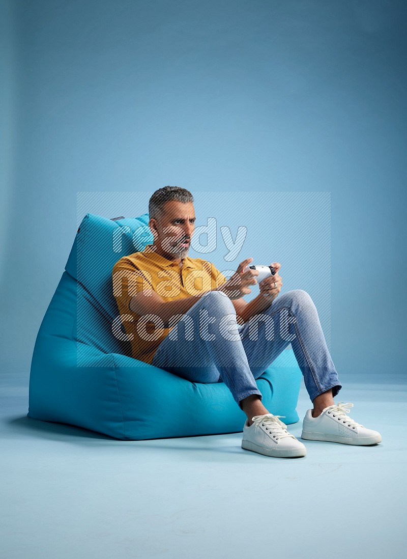 A man sitting on a blue beanbag and gaming with joystick