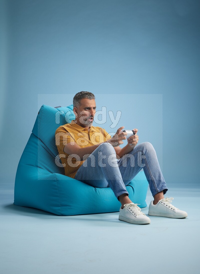A man sitting on a blue beanbag and gaming with joystick