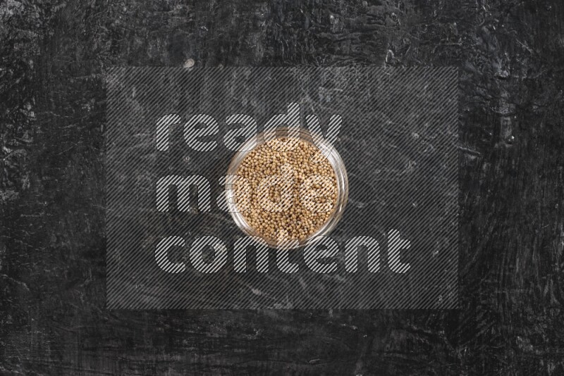 A glass jar full of mustard seeds on a textured black flooring
