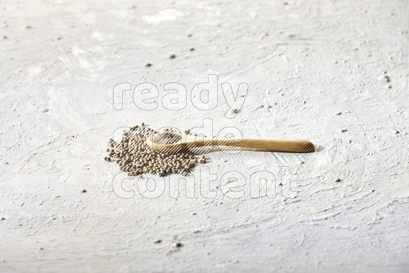 A wooden spoon full of white pepper powder and white pepper beads on textured white flooring