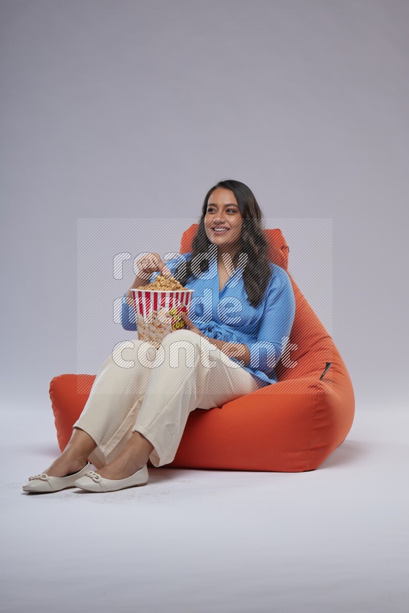A woman sitting on an orange beanbag and eating popcorn