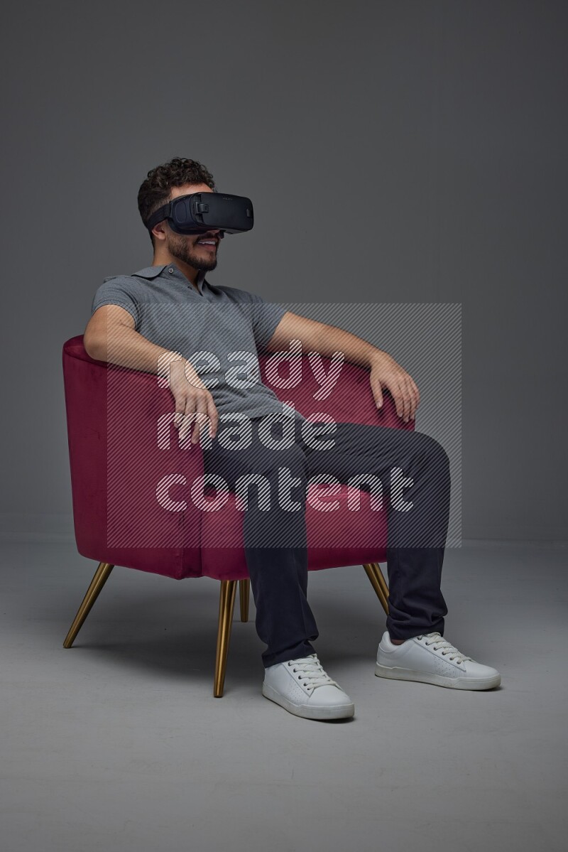 A man wearing casual and wearing VR while sitting on a burgundy chair eye level on a gray background