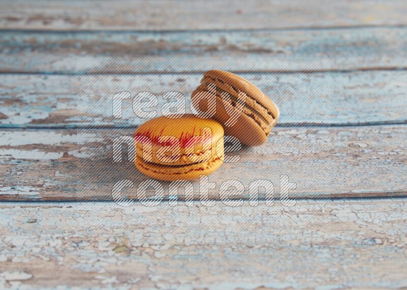 45º Shot of of two assorted Brown Irish Cream, and Orange Exotic macarons on light blue background