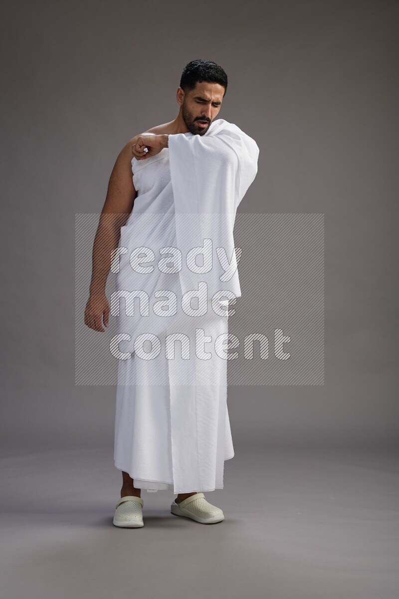 A man wearing Ehram standing showing how to sneeze on gray background