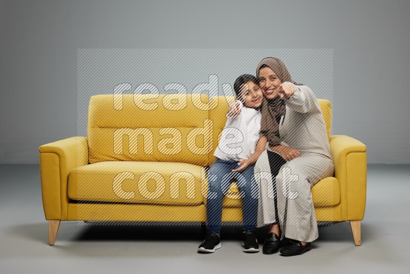 A girl with her mother sitting and interacting with the camera on gray background