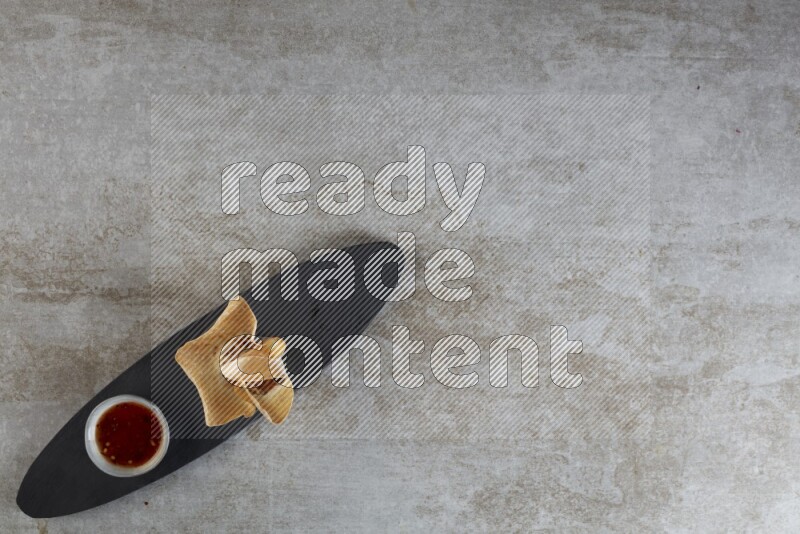 wonton cups with soy sauce ramkin on oval slate on grey textured counter top