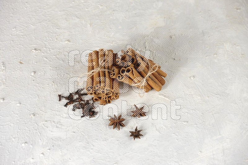 Two bounded stacks of cinnamon sticks with cloves and star anise on white background