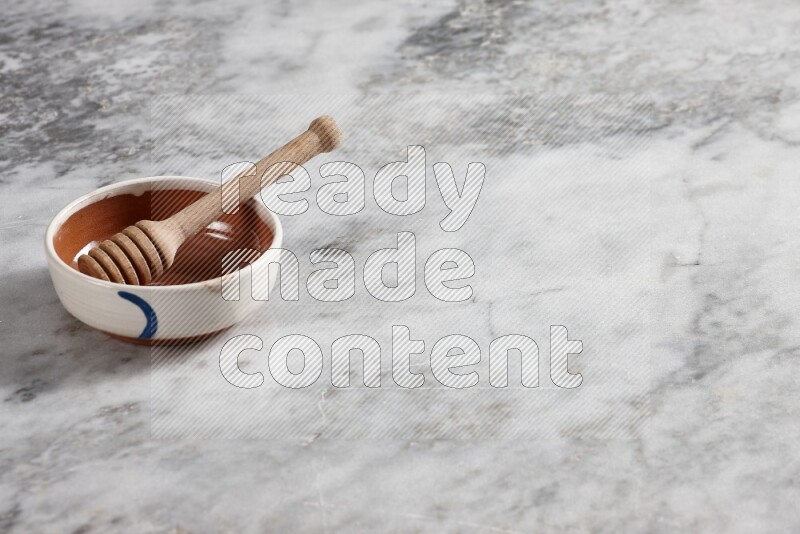 وعاء فخاري متعدد الألوان مع ملعقة عسل خشبية بداخله على خلفية من الرخام الرمادي