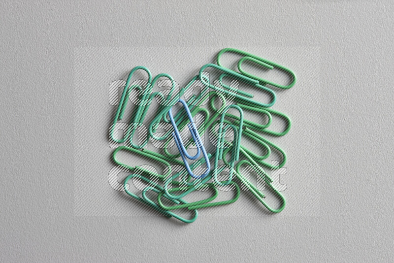 A bunch of green paper clips with a different colored paper clip in the center on grey background