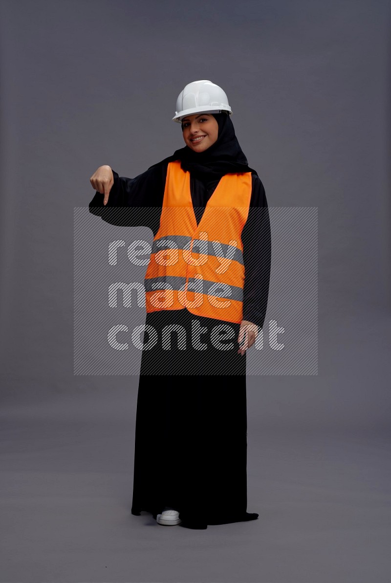 Saudi woman wearing Abaya with engineer vest standing interacting with the camera on gray background