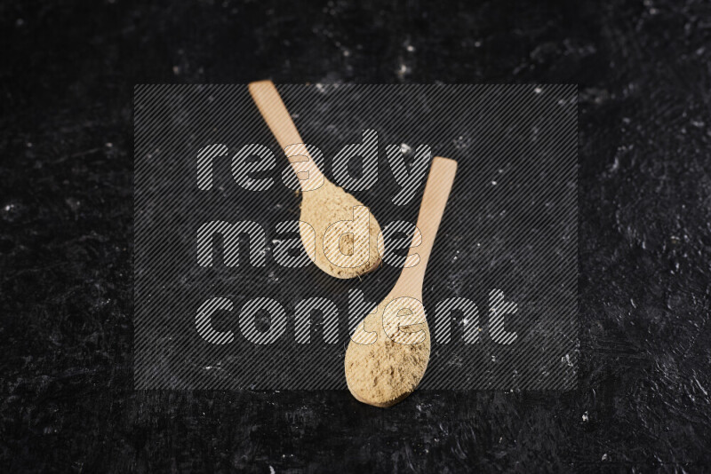 Two wooden spoons full of ground ginger powder on black background