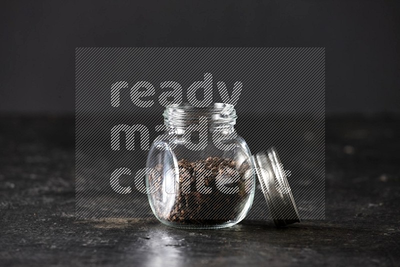 وعاء بهارات زجاجي ممتلئ بحبوب القرنفل على أرضية سوداء