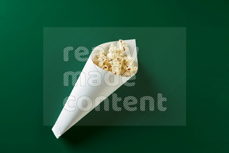 A paper cone full of popcorn on a green background in a top veiw shot