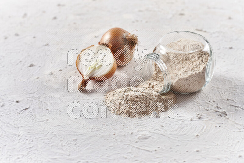 A glass jar full of onion powder flipped with some spilling powder on white background