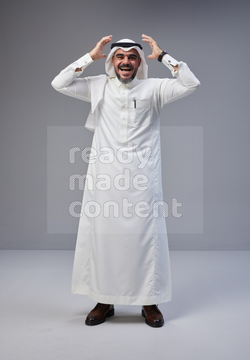 Saudi man Wearing Thob and white Shomag standing interacting with the camera on Gray background