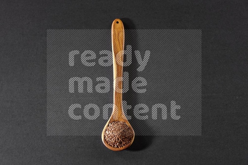 A wooden ladle full of flaxseeds on a black flooring