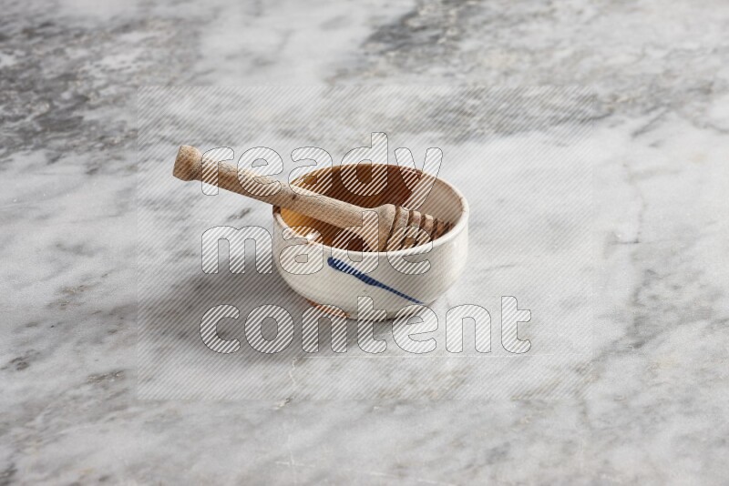 Multicolored pottery bowl with wooden honey dipper in it on grey marble background