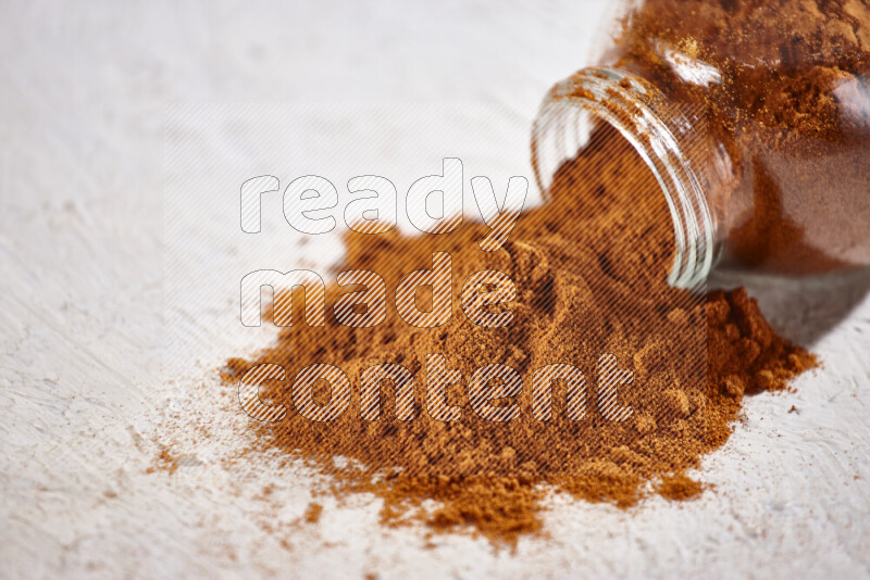 A glass jar full of ground paprika powder flipped with some spilling powder on white background