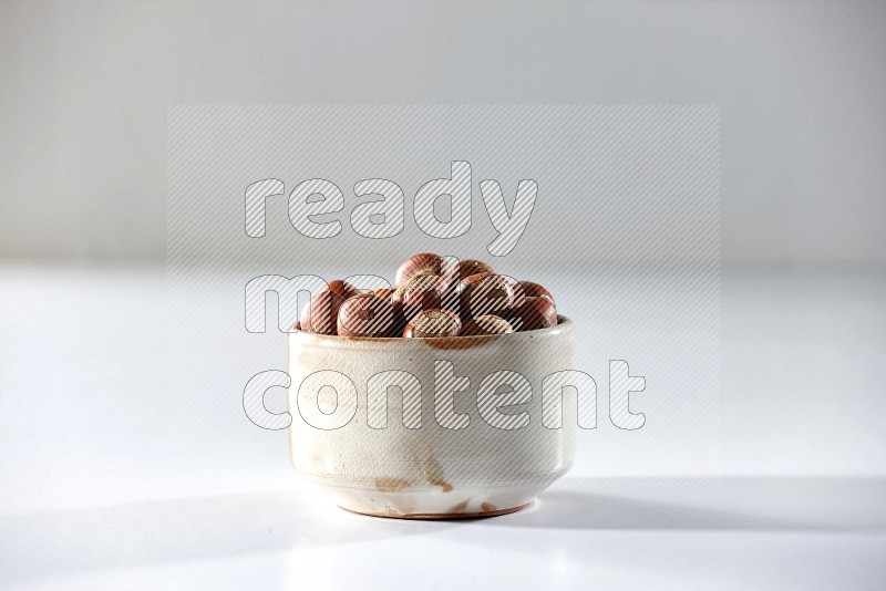 A beige ceramic bowl full of hazelnuts on a white background in different angles