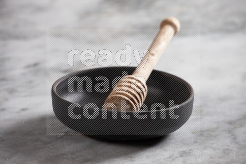 Black pottery bowl with wooden honey dipper in it on grey marble background
