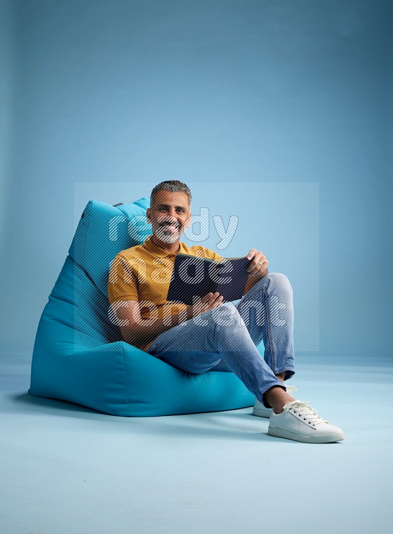 A man sitting on a blue beanbag and reading a book