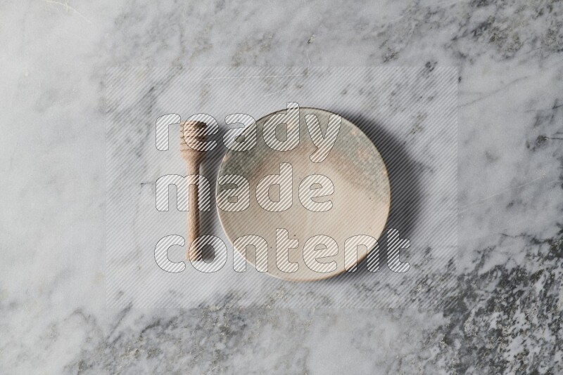 Multicolored pottery plate with wooden honey dipper on the side on grey marble background