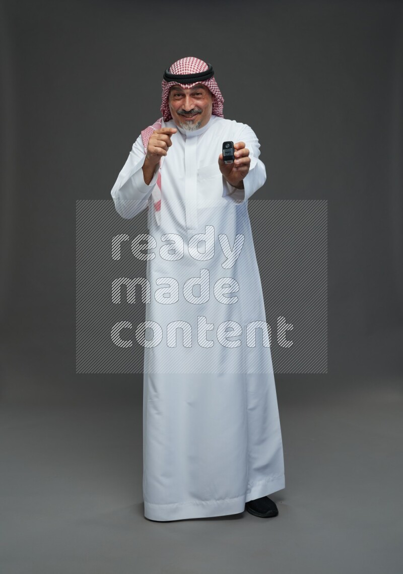 Saudi man with shomag Standing holding car key on gray background