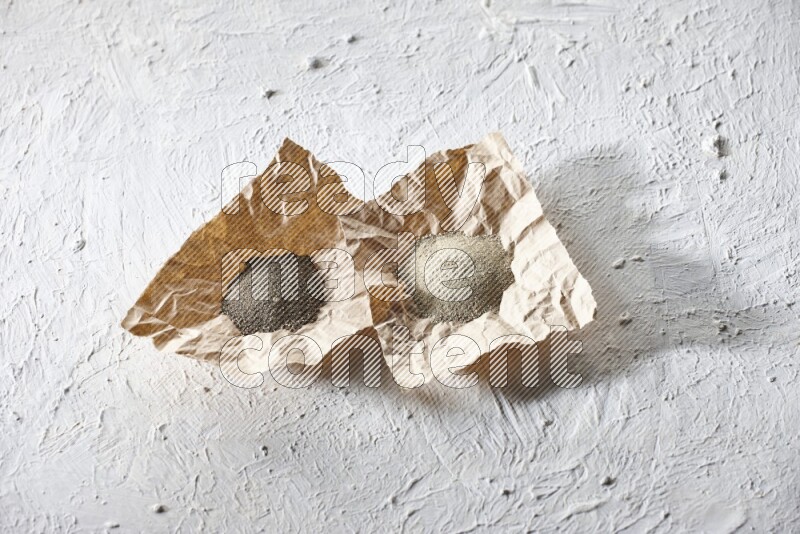 2 Crumpled pieces of paper full of black and white pepper powder on a textured white flooring