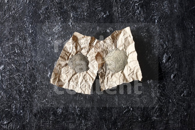 2 Crumpled pieces of paper full of black and white pepper powder on a textured black flooring