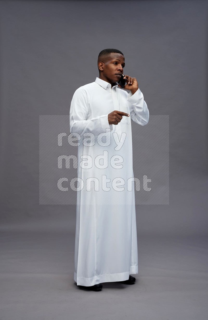 Saudi man wearing thob standing talking on phone on gray background