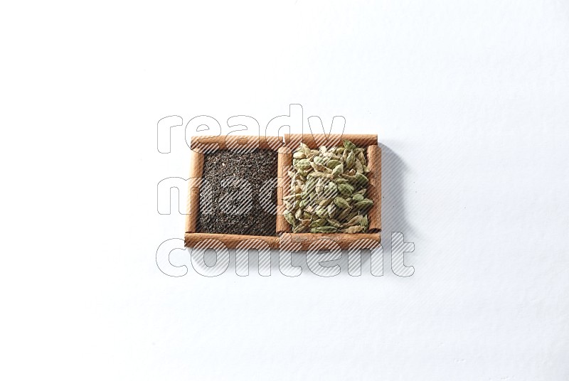مربعان من أعواد القرفة ممتلئان بالشاي الأسود وحبوب الهال علي خلفية بيضاء