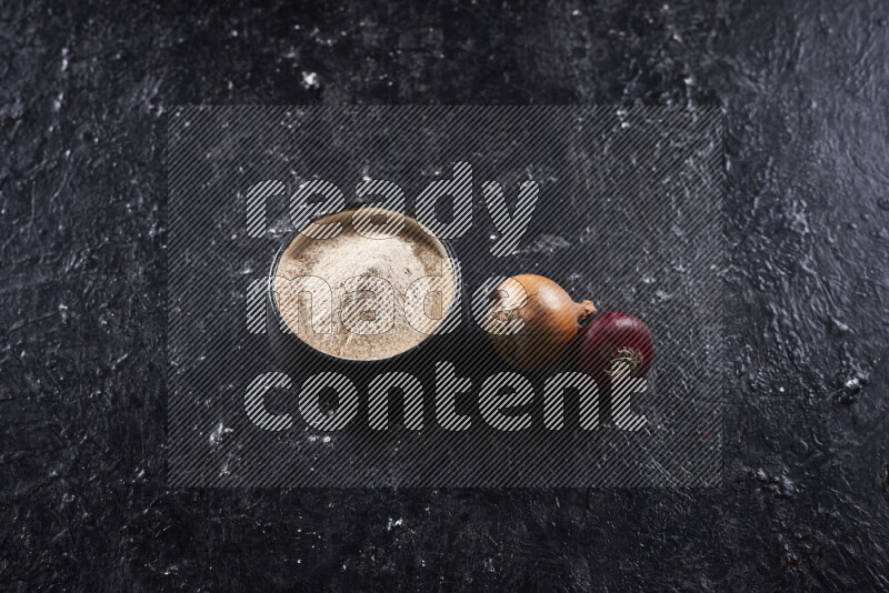 A black pottery bowl full of onion powder on black background