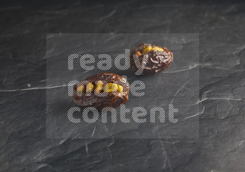 two pistachios stuffed madjoul dates on a black textured background