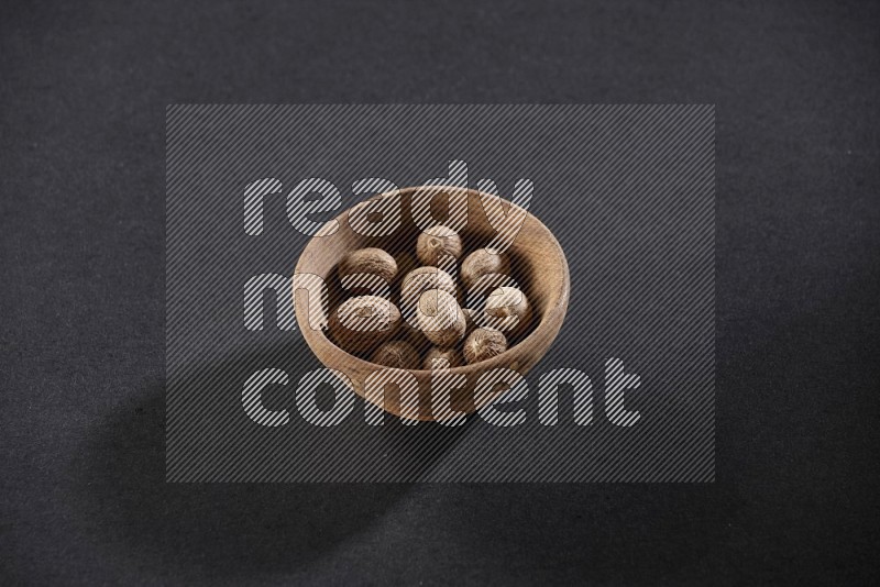 A wooden bowl full of nutmeg on a black flooring in different angles