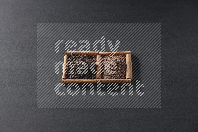 مربعان من أعواد القرفة ممتلئان ببذور الكتان والقرنفل علي خلفية سوداء