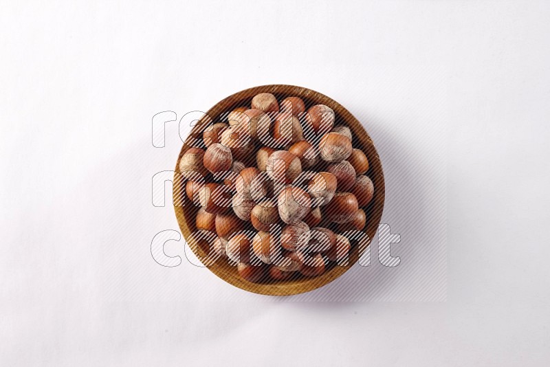 Hazelnuts in a wooden bowl on white background