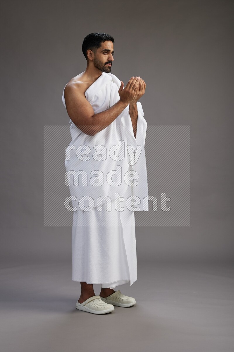 A man wearing Ehram Standing performing dua'a on gray background