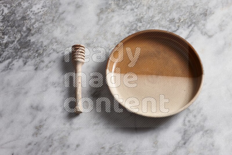 Multicolored pottery oven plate with wooden honey dipper on the side on grey marble background