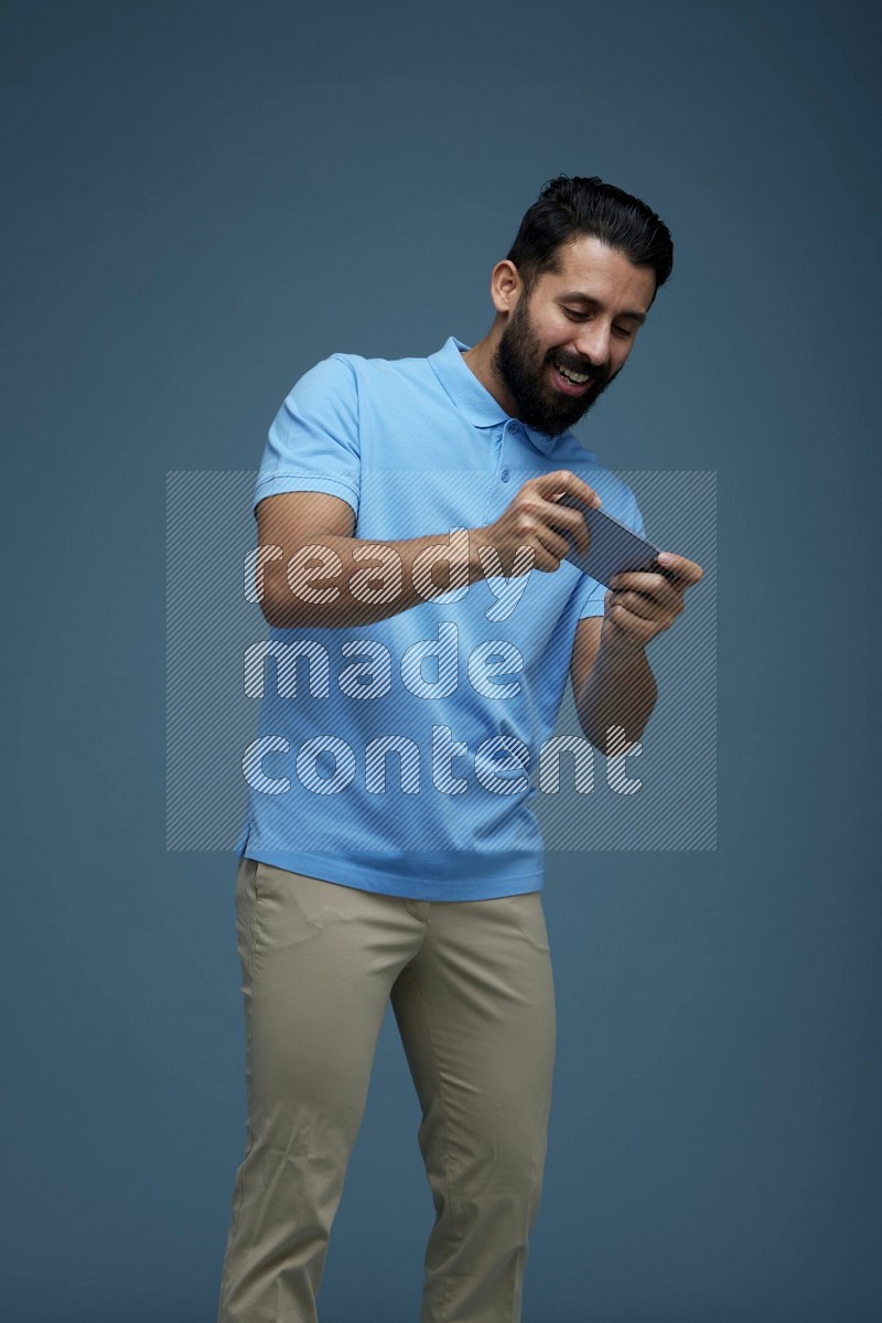 Man playing a game on his phone in a blue background wearing a Blue shirt
