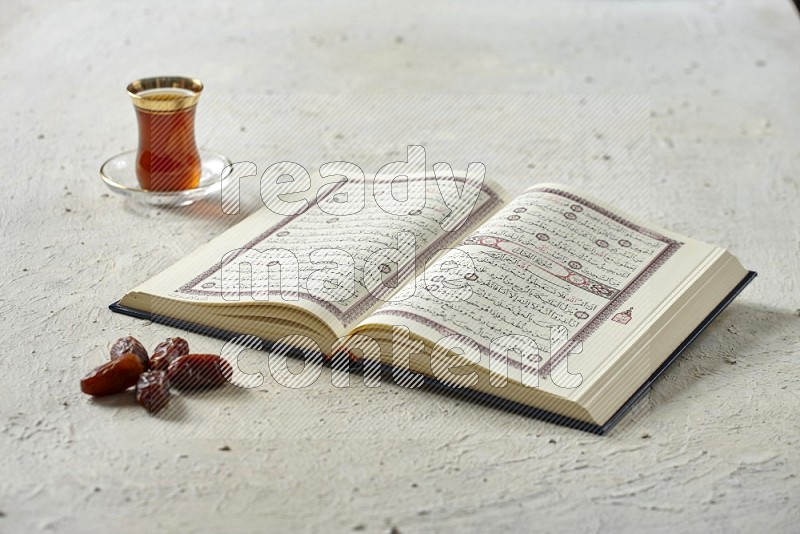 Quran with dates, prayer beads and different drinks all placed on textured white background