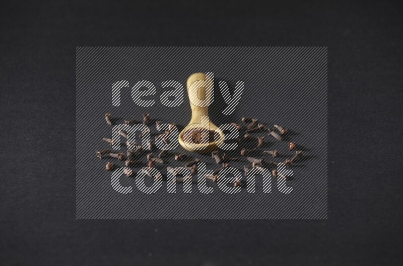 ملعقة خشبية ممتلئة ببودرة القرنفل مع حبوب القرنفل المتناثرة على خلفية سوداء